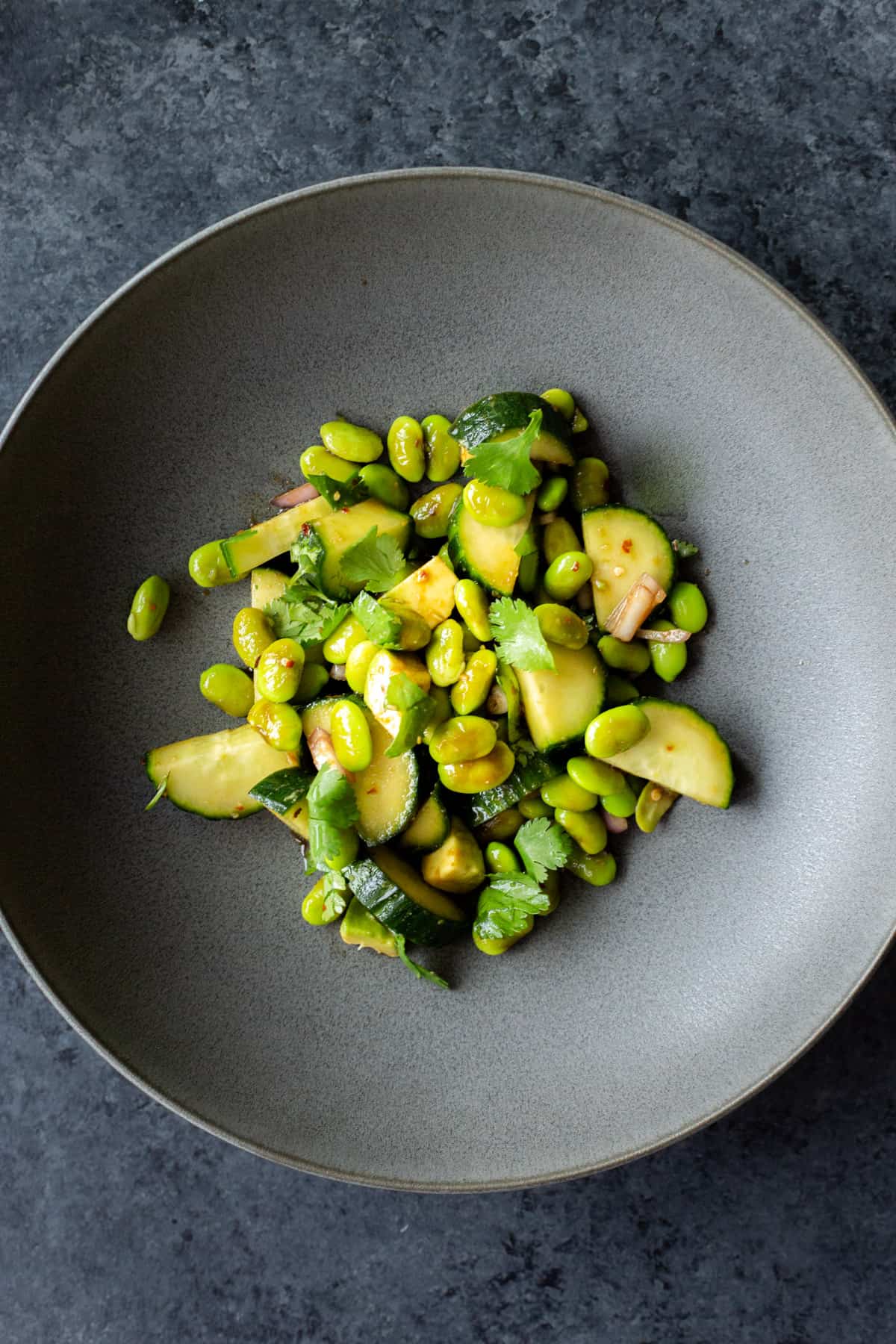 a cucumber, edamame, avocado salad in a grey bowl on a dark background