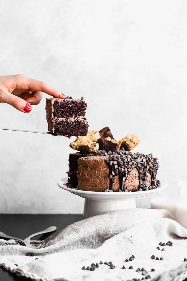 holding a slice of cake next to a cake on a cake stand
